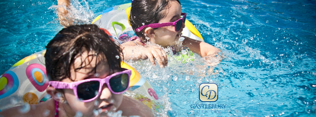Two children wearing sunglasses swimming and playing in a bright blue pool together.