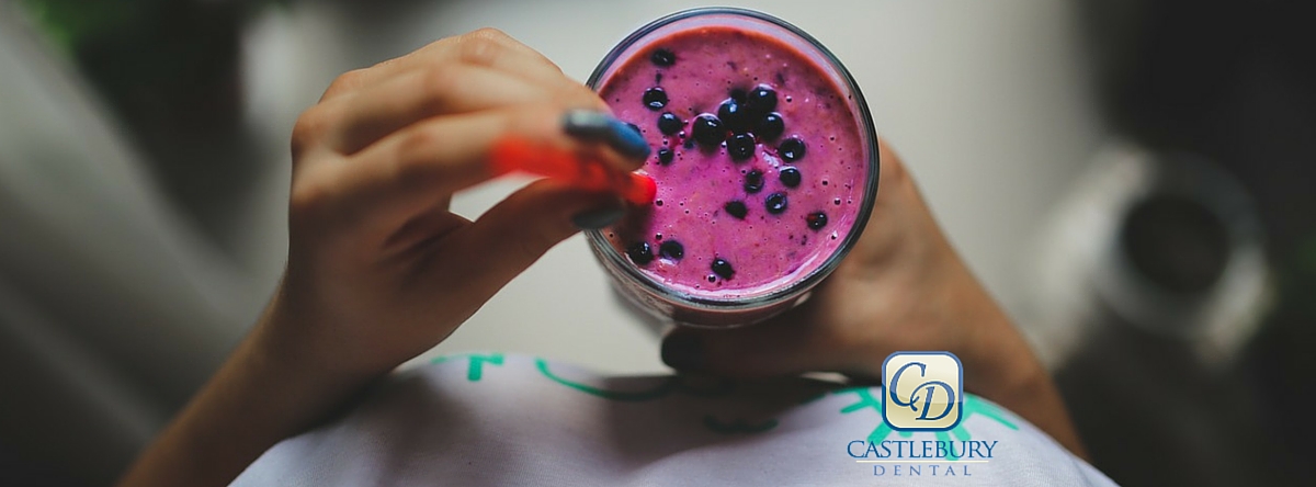 Person holding vibrant purple smoothie or beverage in clear glass cup outdoors.