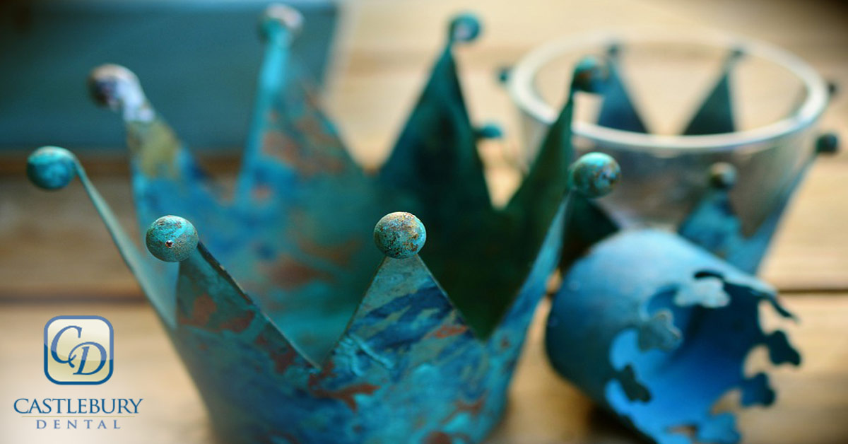 Blue dental crown model displayed on wooden surface with Castlebury Dental logo visible.
